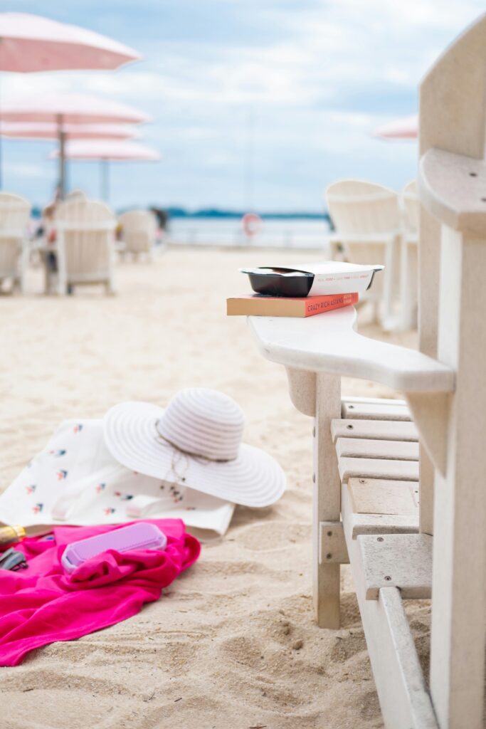A serene beach scene with an armchair, sun hat, and book on a sandy shore, capturing summer vibes.
