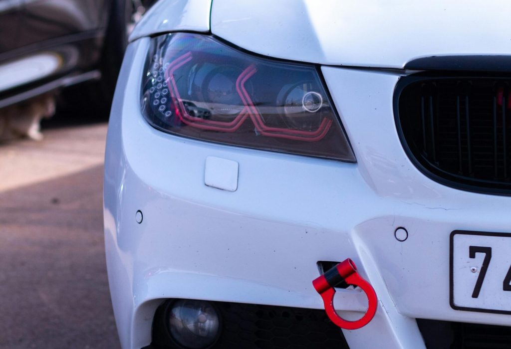 Detailed view of a white car's front headlight and bumper in daylight, ideal for automotive themes.
