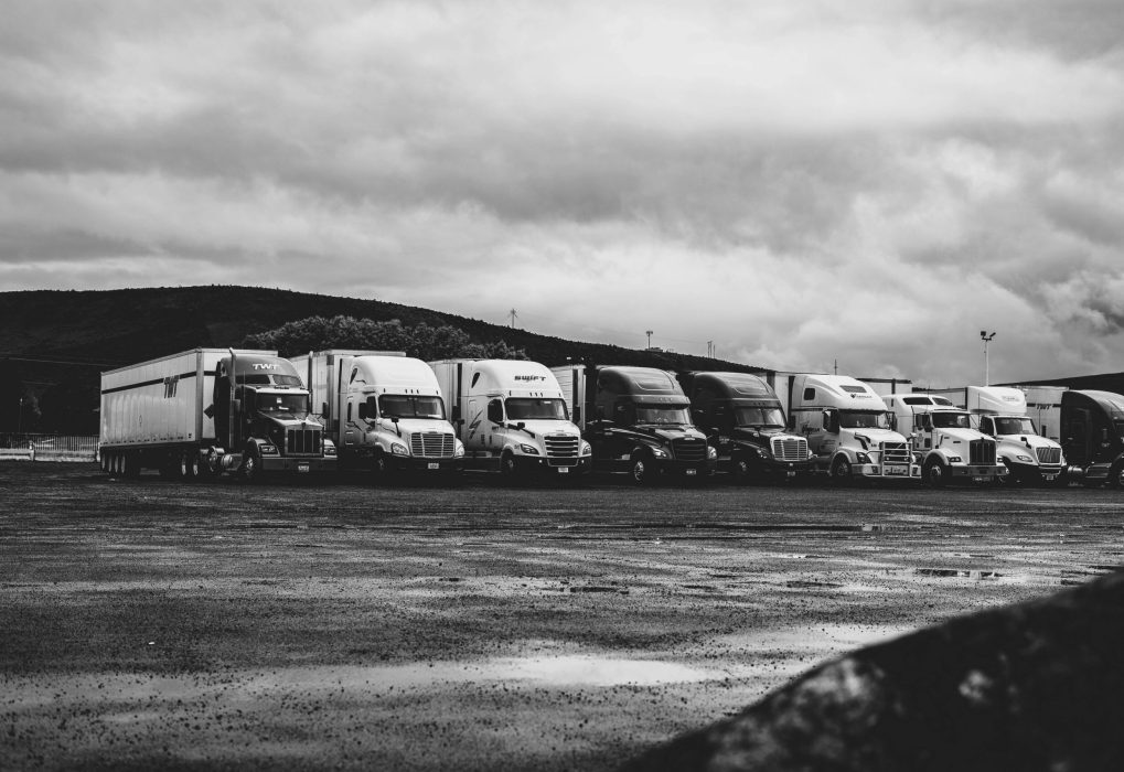 Row of parked semi trucks in a rainy lot, captured in a dramatic black and white setting.