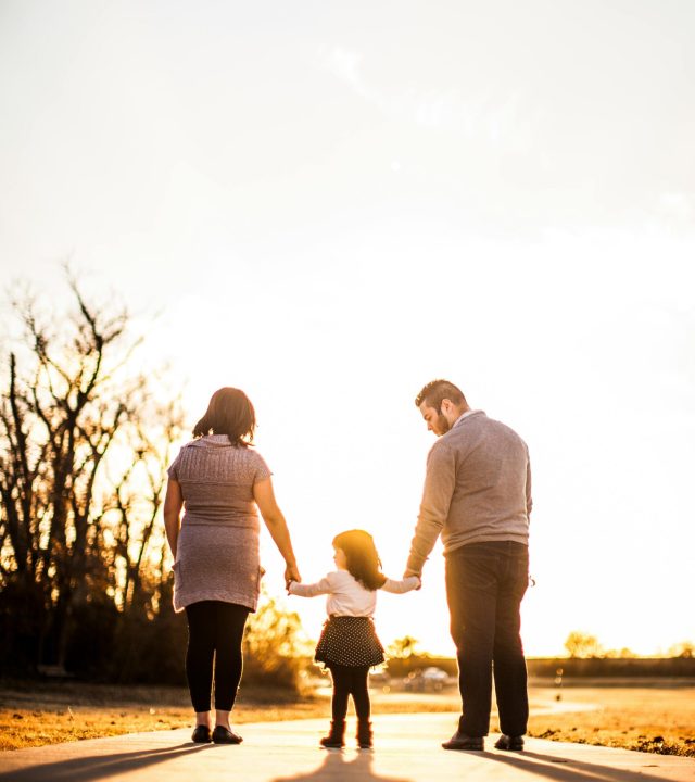 A family of three walks hand in hand at sunset, enjoying togetherness and warmth.