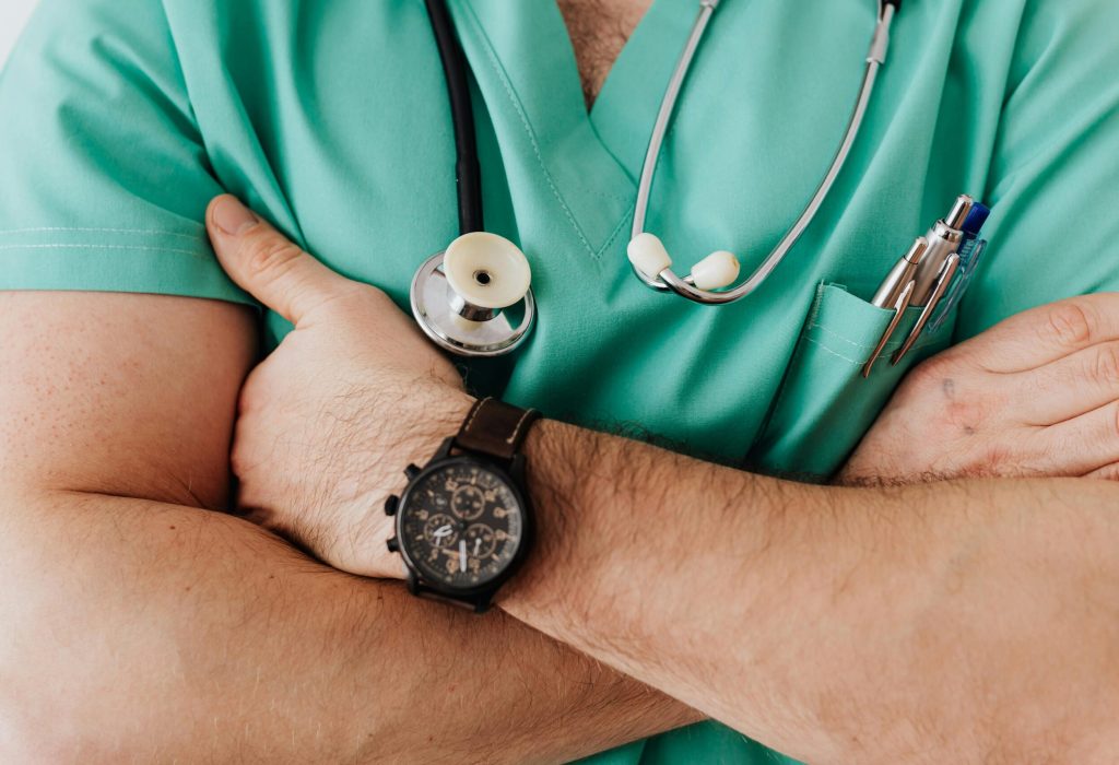 Close-up of a healthcare professional with arms crossed wearing medical scrubs and stethoscope.