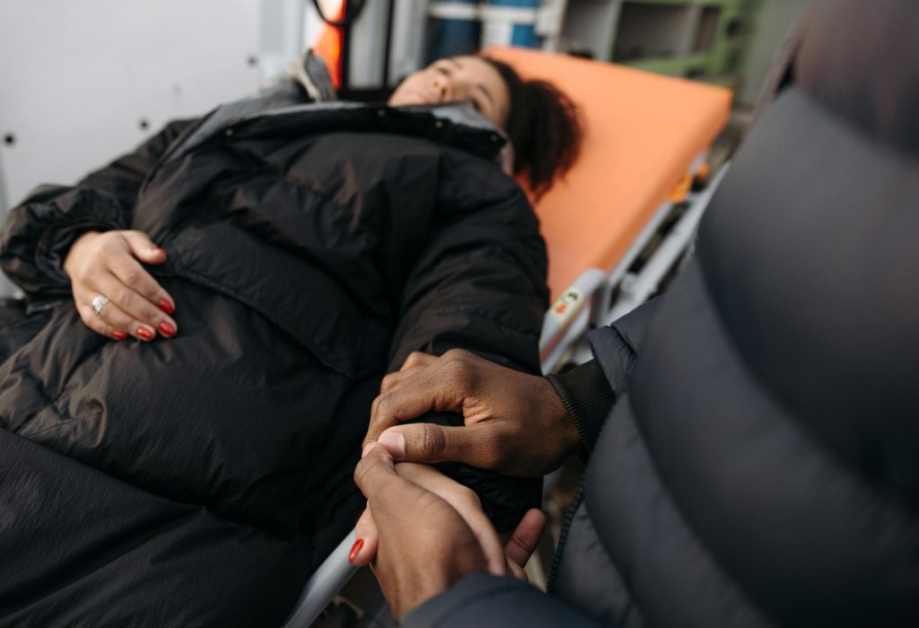 A woman lying on a stretcher as a comforting hand holds hers. Indoor medical care scene.