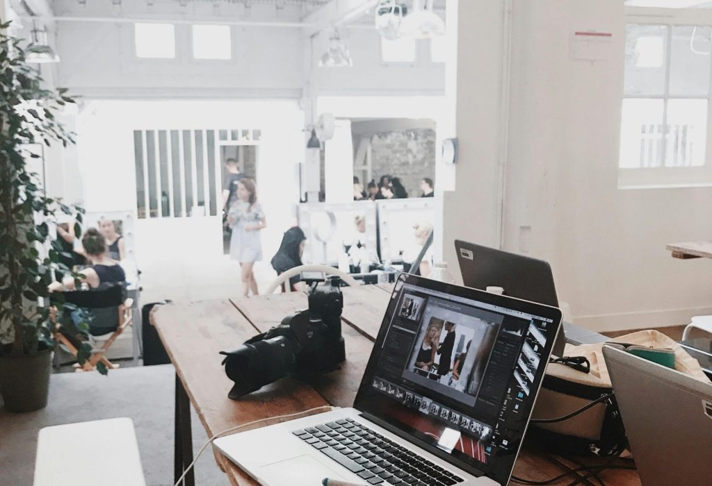 A bright, modern workspace featuring laptops, a camera, and a drawing tablet in an indoor office.
